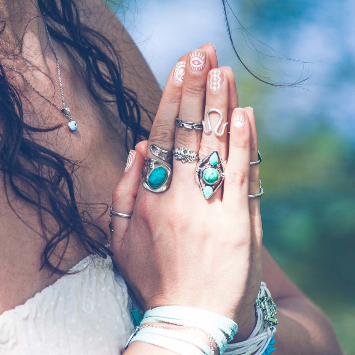 Close-up of hands with multiple rings, including turquoise stones, against a blurred natural background.