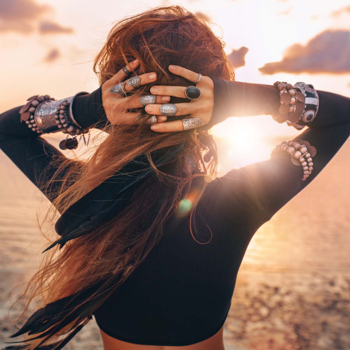 A woman with hands behind her head, facing a sunset over water, representing psychic Lemurian spiritual awareness.