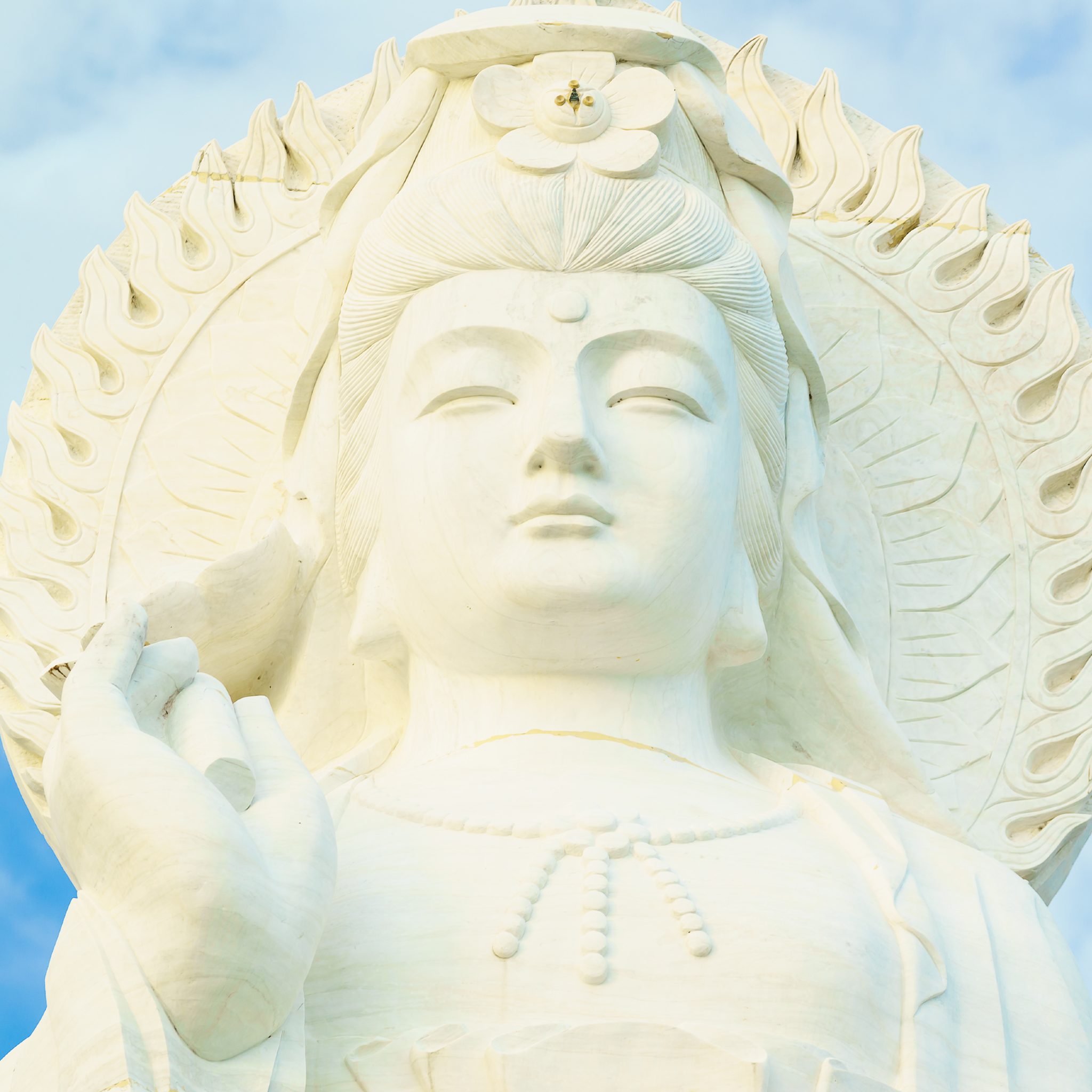 White marble Quan Yin statue with intricate details against a clear blue sky.