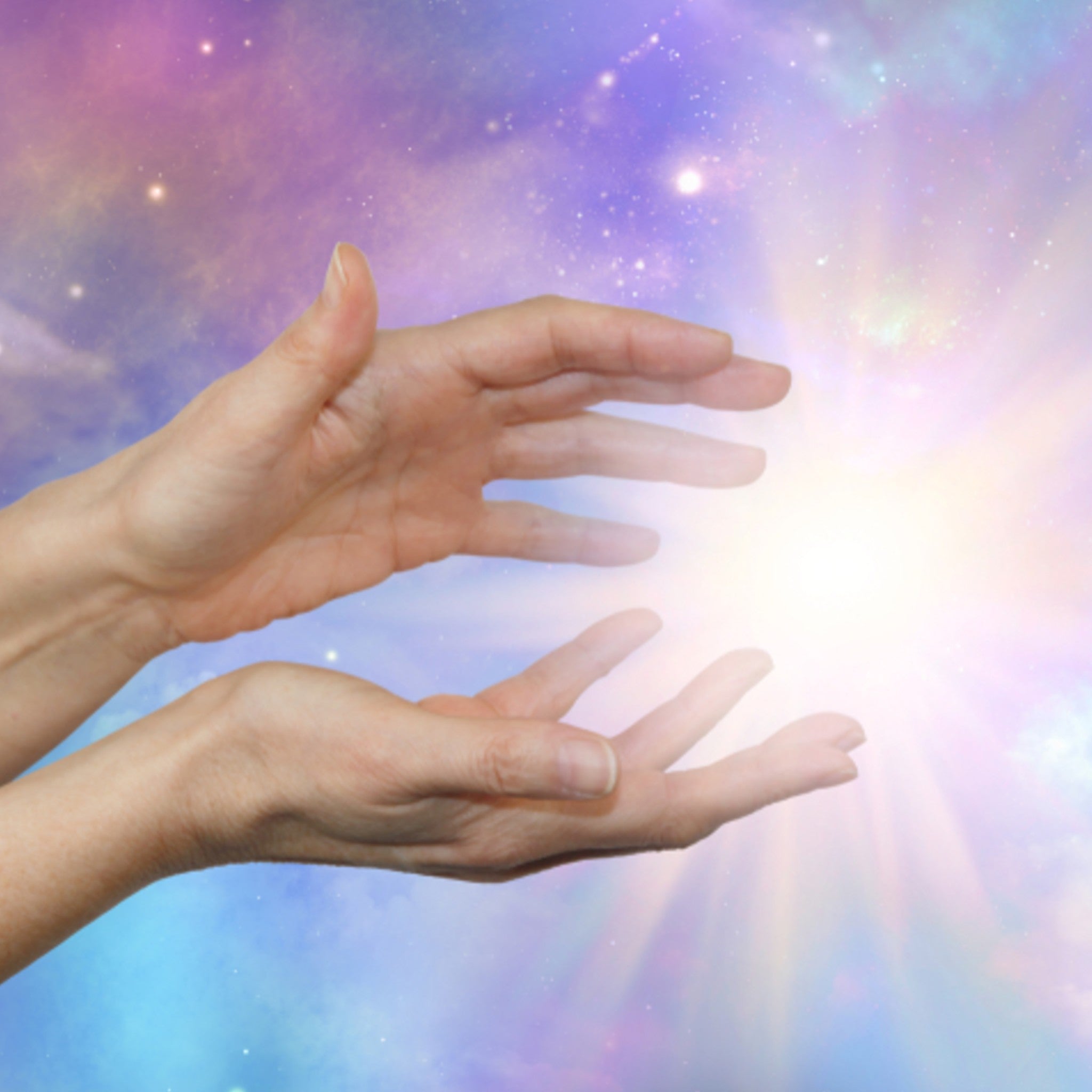 A close-up photograph of a pair of hands held in a receiving or channelling gesture, with a bright white light bursting forth from between them. The background is a dreamy celestial scene with soft pink, purple, and blue colours and shimmering stars, symbolising powerful Reiki energy.
