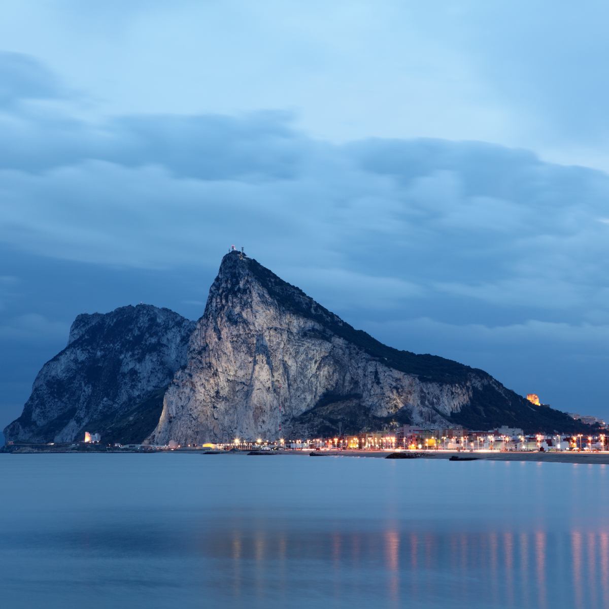 Rock of Gibraltar at dusk with lights reflecting on the water.