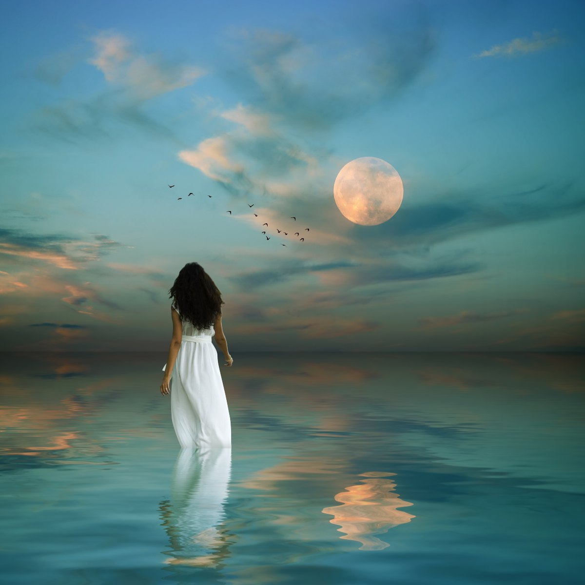 Woman in a white dress walking into calm water towards a large full moon under a dusk sky with flying birds.