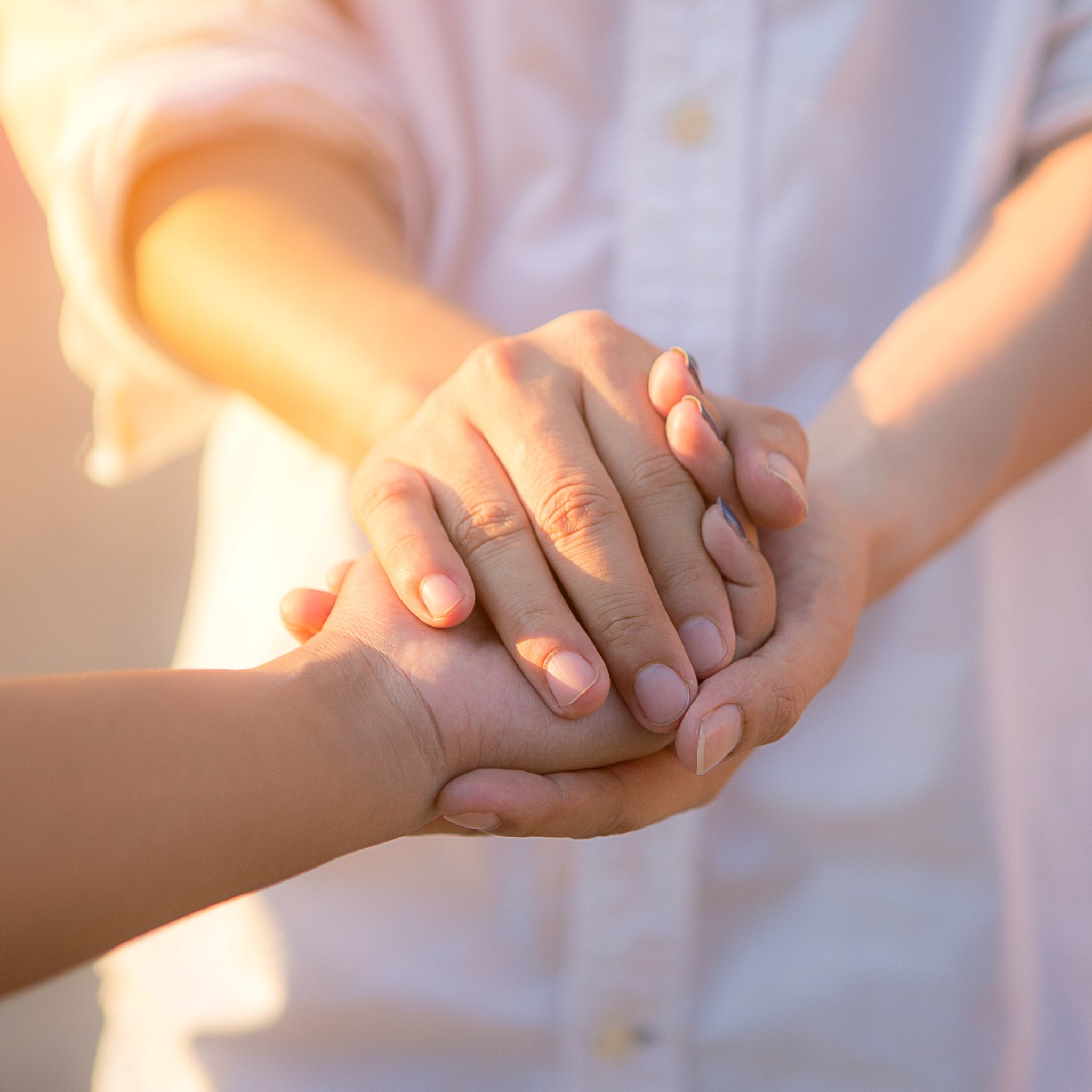 Two pairs of hands holding each other with a warm, blurred background representing the service rite.