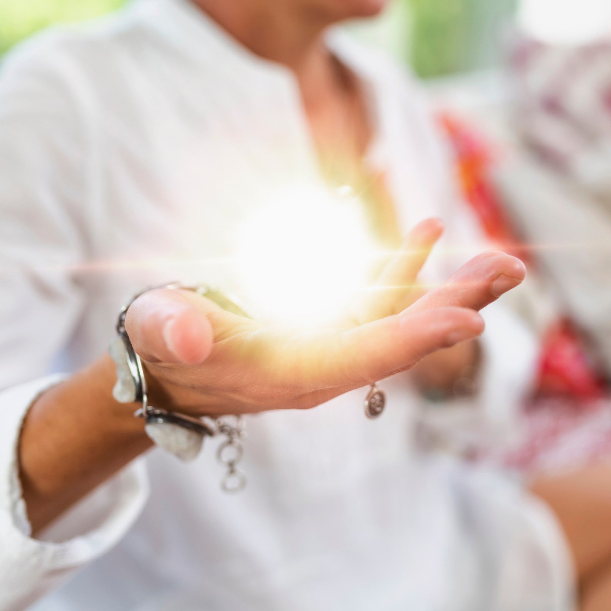 A close-up of a hand gently holding a glowing orb of bright white light and sparkles, symbolising the spiritual awareness rite.