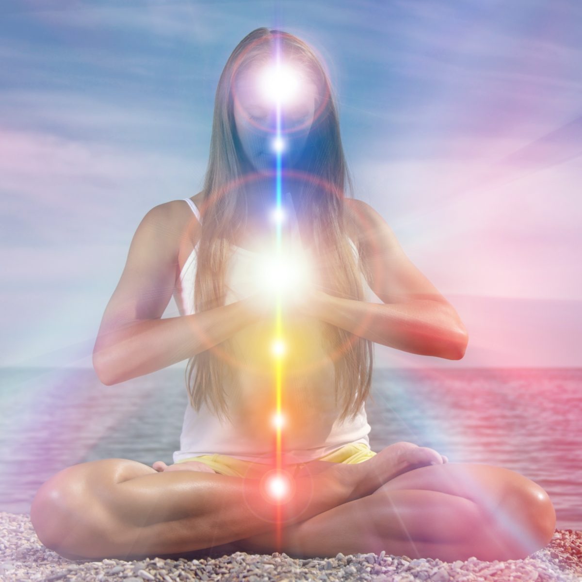 Person meditating on a beach with an illuminated, vertically aligned column of chakras and kundalini spiritual light.