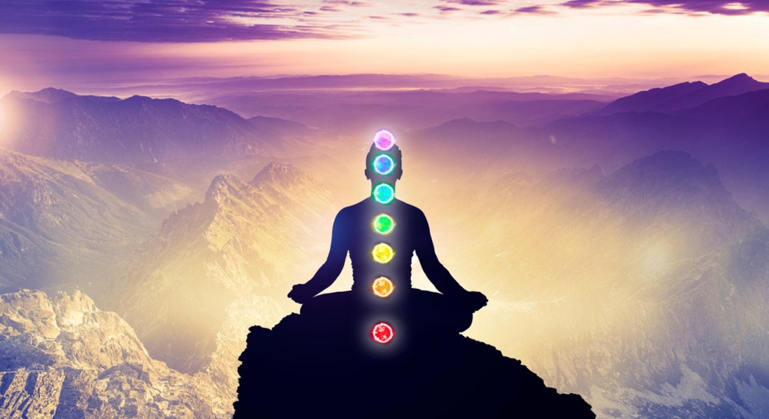 Person meditating with chakra colours on a mountain at sunset, suggesting potential for well-being offered by distant healing treatments.