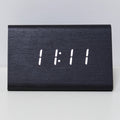 A minimalist black wooden digital clock displaying the number '11:11' in white LED light, resting on a white surface.