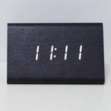 A minimalist black wooden digital clock displaying the number '11:11' in white LED light, resting on a white surface.