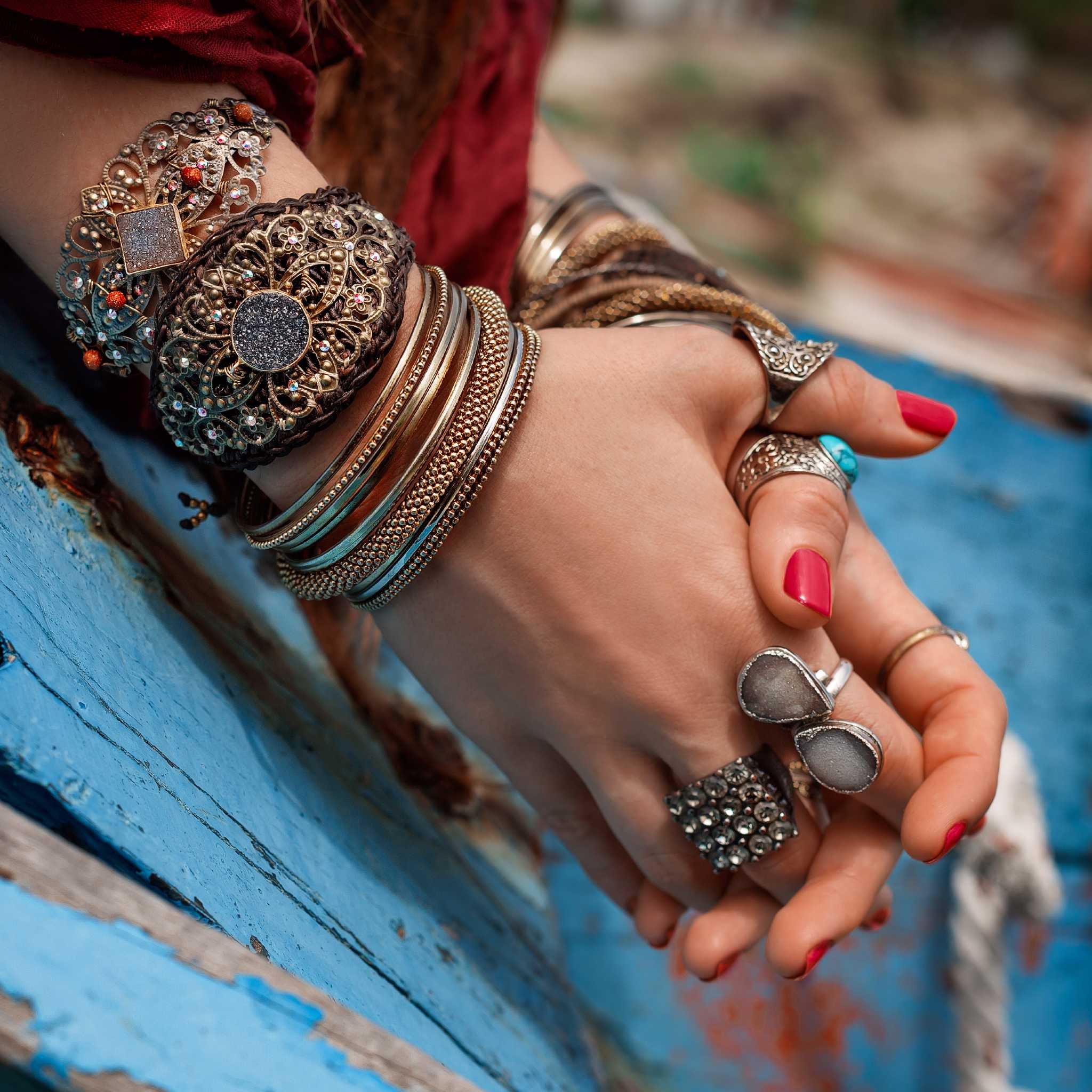 Close-up of a person's hands covered in intricate, stacked gold and silver rings and bangles, resting on a weathered blue wooden surface.