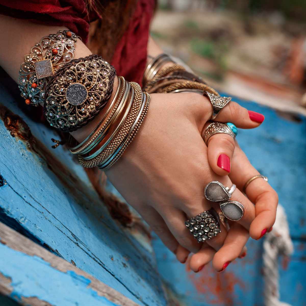 Close-up of a hand with multiple abundant bracelets and rings on a blue surface.