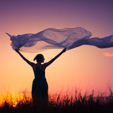 Woman holding a flowing fabric against a sunset sky symbolising elemental air.