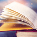 Close-up of a large, opened book with pages illuminated by a warm, ethereal light and golden bokeh sparkles.