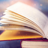 Close-up of a large, opened book with pages illuminated by a warm, ethereal light and golden bokeh sparkles.