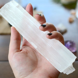 A hand gently holding a long, rectangular piece of white selenite crystal, representing angelic selenite protection.