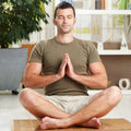 Man peacefully meditating in a living room with plants and furniture in the background.