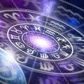 A deep space image featuring a glowing white circle containing the twelve symbolic signs of the Zodiac or astrology wheel, overlaid against a backdrop of stars, nebulae, and a partial view of a planet in the lower right. A bright, violet-hued light emanates from the centre of the wheel, symbolising the spiritual focus of the astrology path alignment dedication.