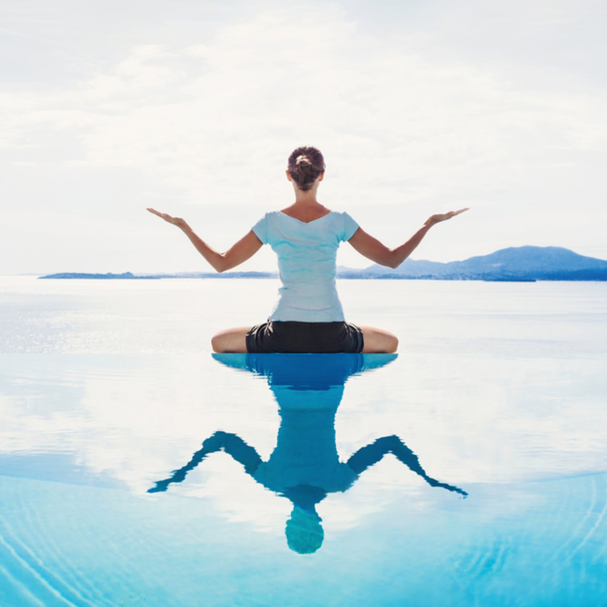 Person in a calm yoga pose on a reflective water surface with mountains in the background.