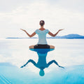Person in a calm yoga pose on a reflective water surface with mountains in the background.