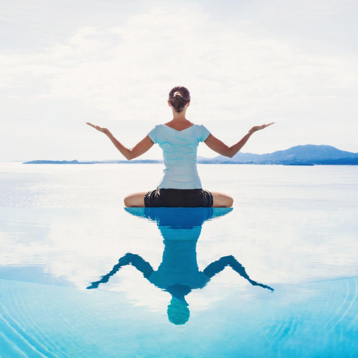 Person in a calm yoga pose on a reflective water surface with mountains in the background.