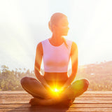 A woman sits in a cross-legged yoga pose with glowing orange-yellow light emanating from her Root Chakra.