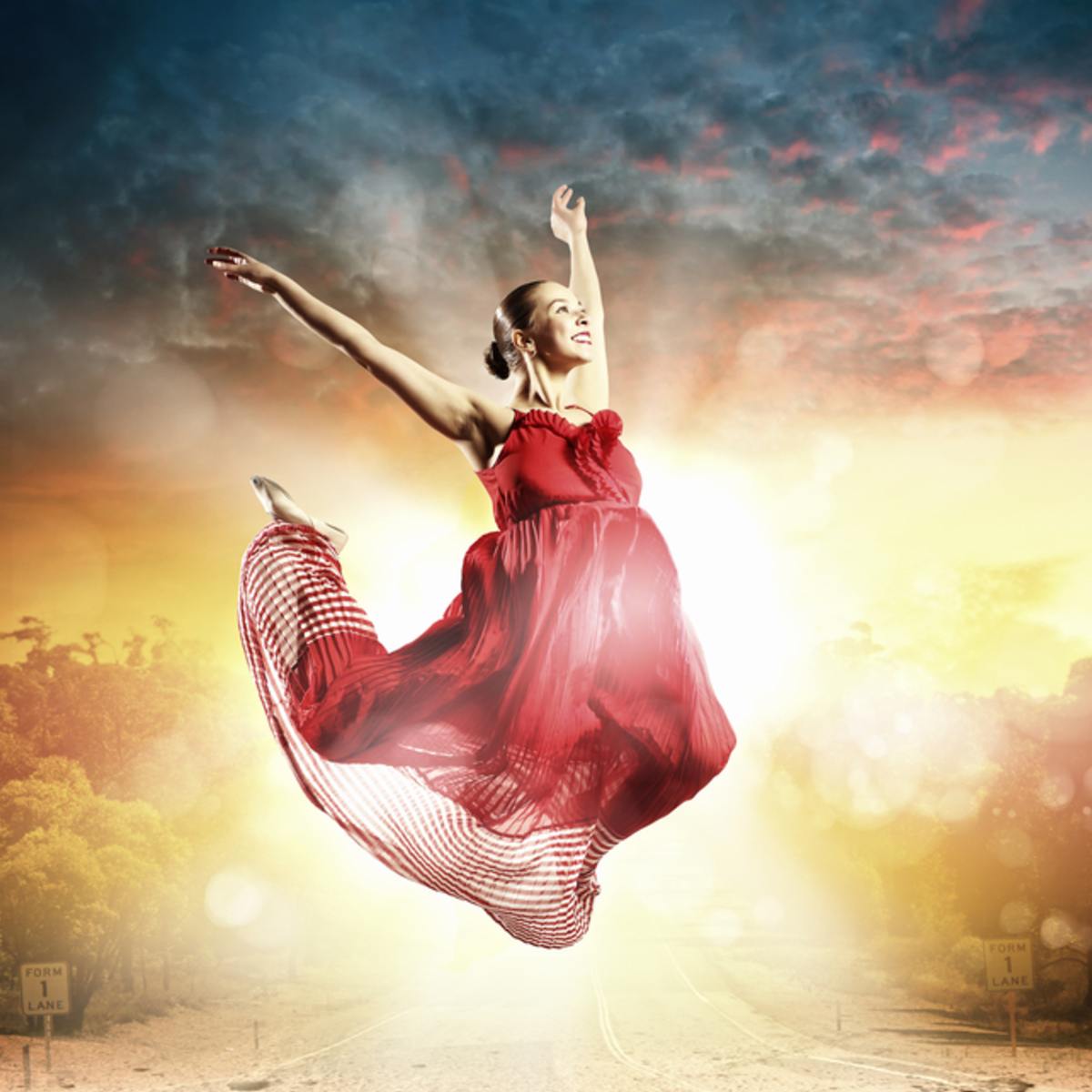 Smiling dancer in a bright red dress performing against a dramatic sky symbolising freedom.