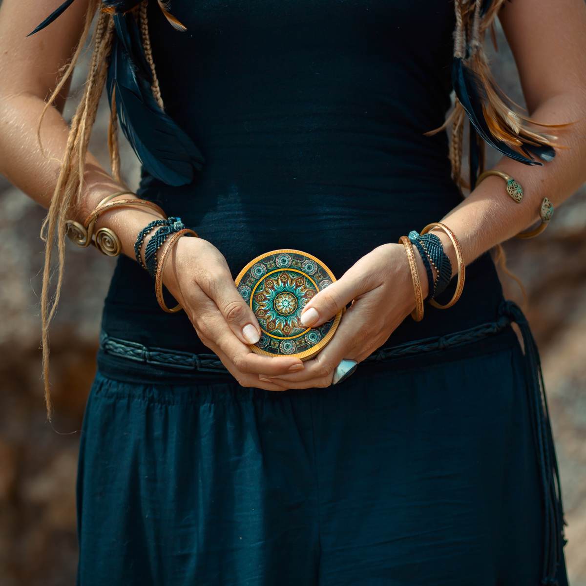 Person holding a decorative object with intricate patterns, wearing dark clothing and multiple bracelets.