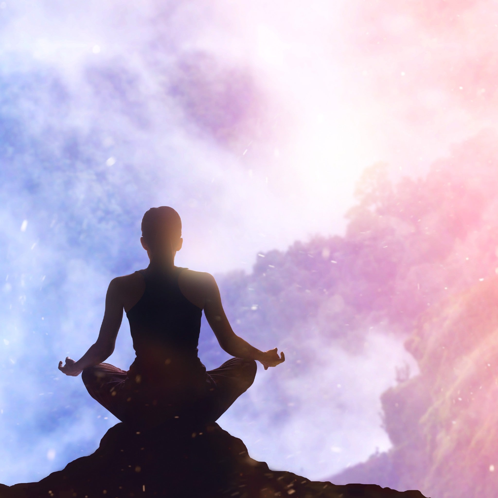 A silhouette of a person meditating on a rocky cliff, looking out over a mountainous, bright, misty valley, representing abundance connections.