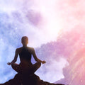Silhouette of a person meditating against a colourful, pink cloudy sky background.