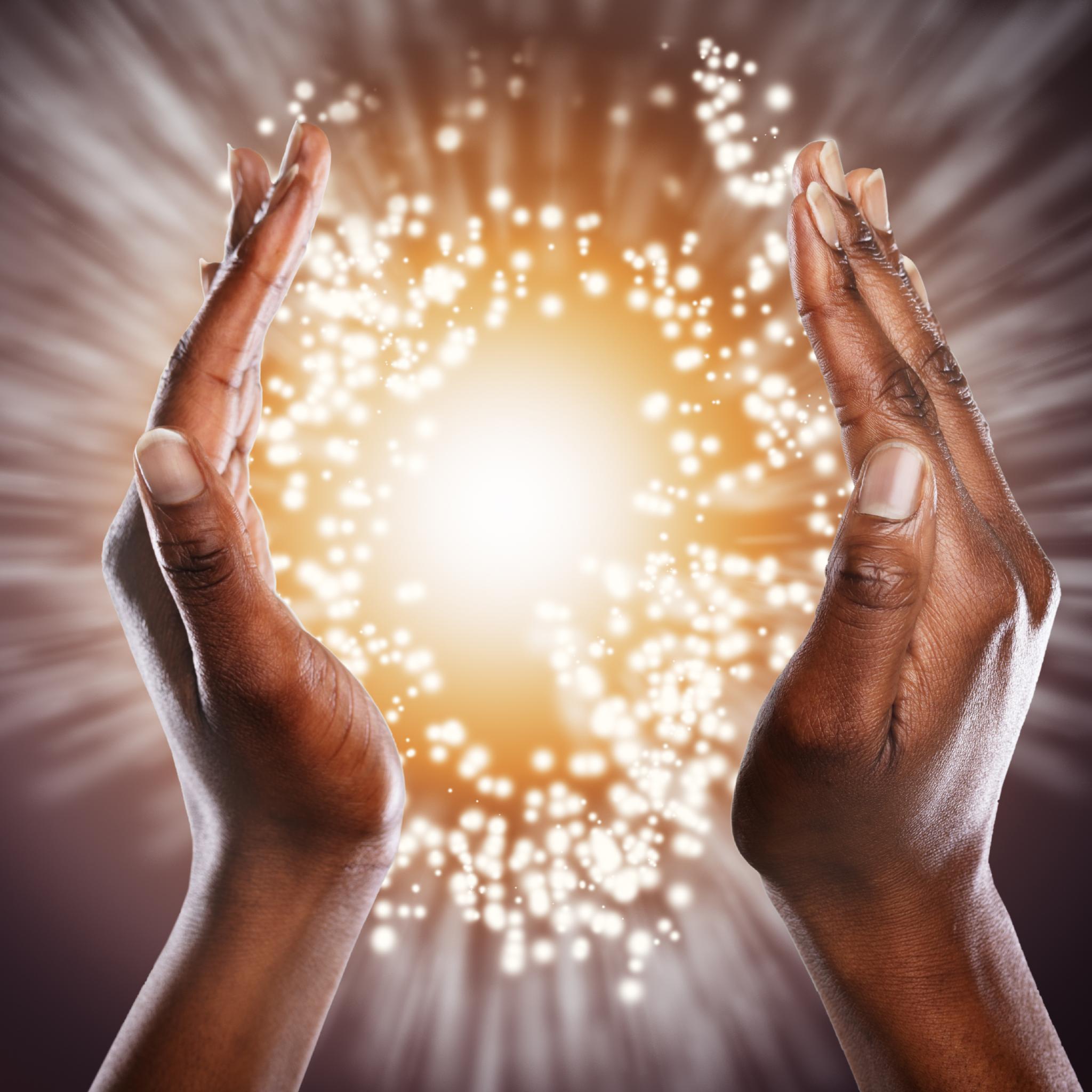 Two hands holding a radiant light source against a dark background glowing background.