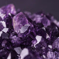 Close-up of deeply saturated purple amethyst crystals on a dark background.