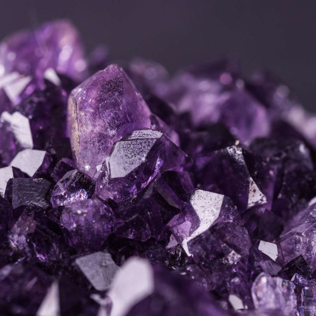 Close-up of deeply saturated purple amethyst crystals on a dark background.