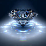 A large, brilliantly cut diamond floating against a dark background, reflecting bright light and creating vibrant rainbow-coloured prismatic flares on the surface below.