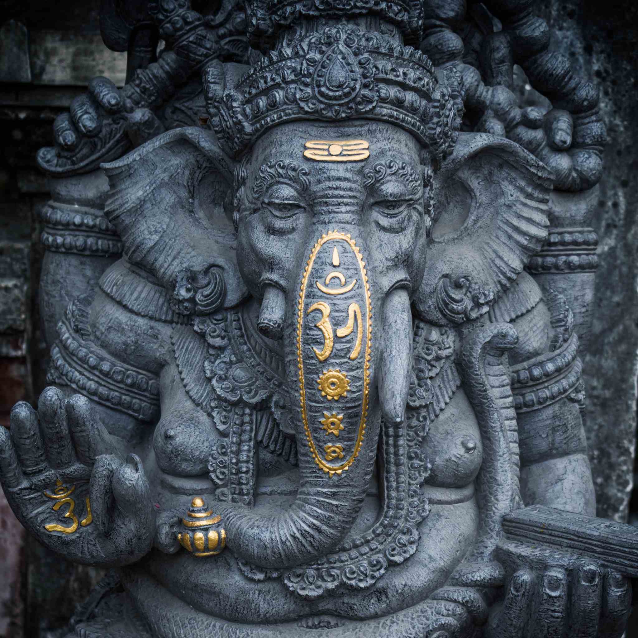 Dynamic Ganesha Connections Maintenance Attunement: detailed grey stone statue of the Hindu deity Ganesha with gold-painted sacred symbols on the trunk and forehead.