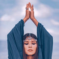 A serene woman with eyes closed, raises her hands in offering above her head with harmonious energy.