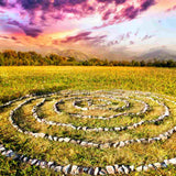 A medicine wheel or labyrinth with a vibrant sunset over distant hills and forest in the background.