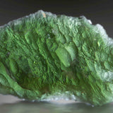 Close-up of a moss green Moldavite crystal with a dark background.