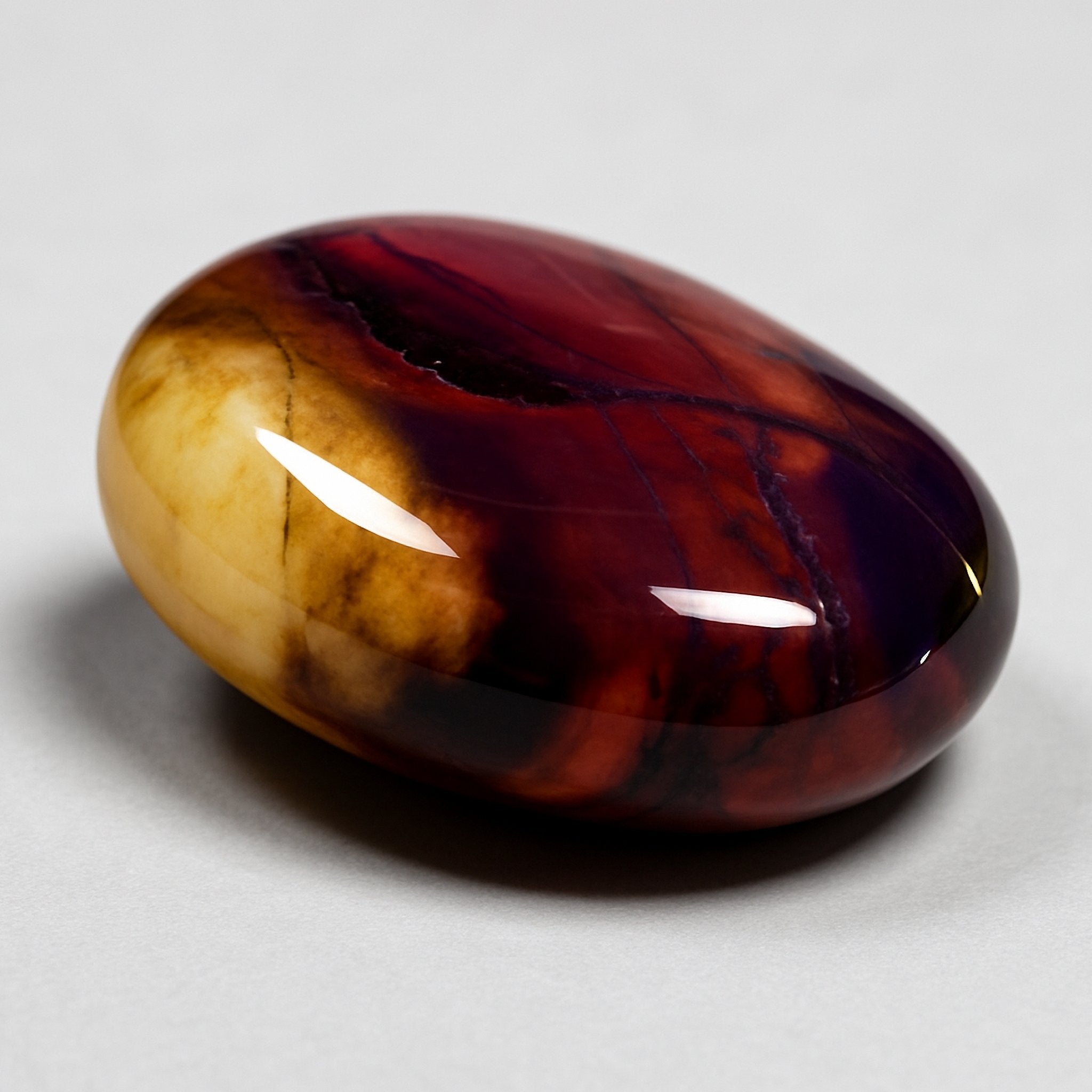 A close-up of a polished, swirling red, yellow, and brown Mookaite gemstone.
