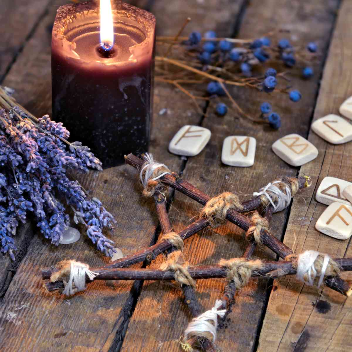 Ritual setup with candles, runes, and herbs on a wooden surface.