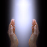 A pair of cupped, open hands reaching up from the bottom of a dark frame, cradling a bright, glowing, white-to-light-purple column of light. The image suggests the receiving or channelling of spiritual energy, illustrating an energy healer performing a treatment.