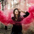 Woman in a black outfit with pink smoke effects in a forest setting.