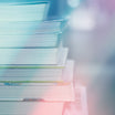 A stacked pile of books, blurred and softly illuminated with a bright, ethereal glow in shades of blue, white, and pink.