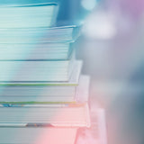 A stacked pile of books, blurred and softly illuminated with a bright, ethereal glow in shades of blue, white, and pink.