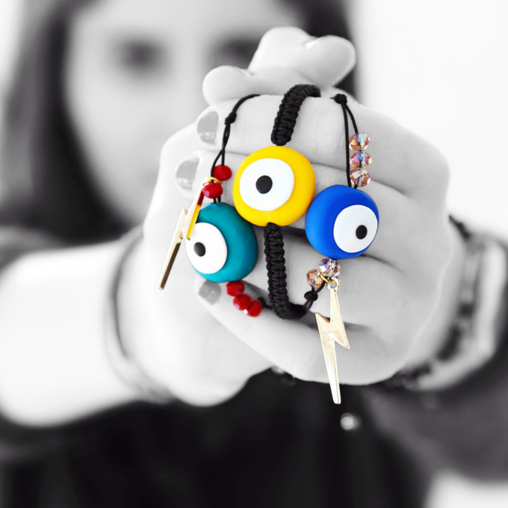A person holding outstretched arms holding colourful evil eye charms on a white background.