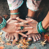 Close-up of bare feet with a green ring and colourful bracelets standing on the ground, grounding on a natural background.