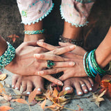 Close-up of bare feet with a green ring and colourful bracelets standing on the ground, grounding on a natural background.