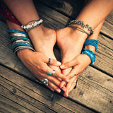 A close-up of a person's bare feet and hands adorned with many silver and blue bracelets signifying grounding.
