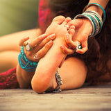 Person with multiple bracelets and rings holding their feet on a wooden surface.