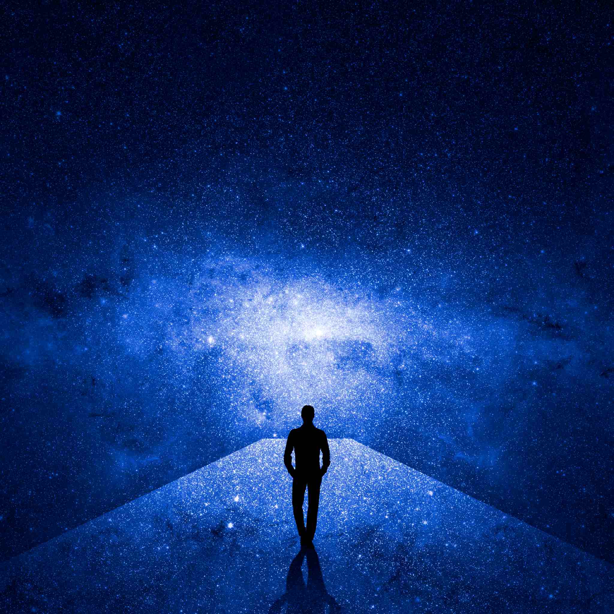 Silhouette of a person standing on a path leading to a bright blue galaxy.