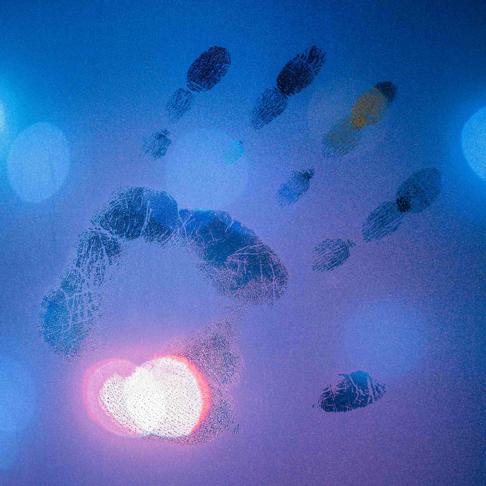 A handprint left on a blue, misty or frosted glass surface, with a glowing red and white heart-shaped light illuminating the palm area from beneath.
