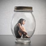 Person sitting inside a glass jar with a metal lid on a neutral background represents inappropriate fear.